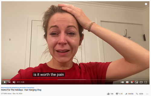 Screenshot from Lindsey Stirling's hair hanging vlog, captioned 'Is it worth the pain?'